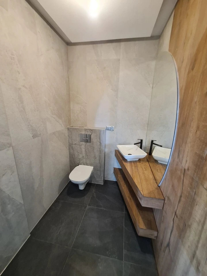 Wykończona przez SB House łazienka. Zabudowana toaleta, umywalka położona na drewnianej półce, piękne podświatlane lustro